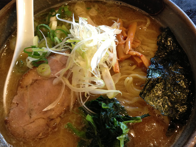 少し濁った茶色のスープに麺と白髪ねぎなどのトッピングが載ったラーメン