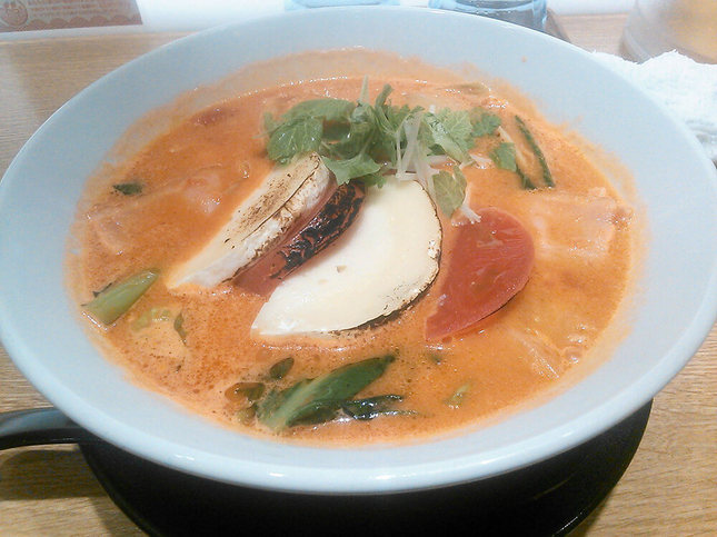 オレンジ色のトマトベースのスープに麺と野菜などのトッピングが載ったラーメン