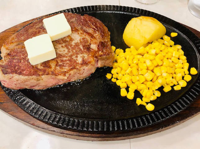鉄板に乗った分厚いステーキとバター二欠片とコーンとポテト