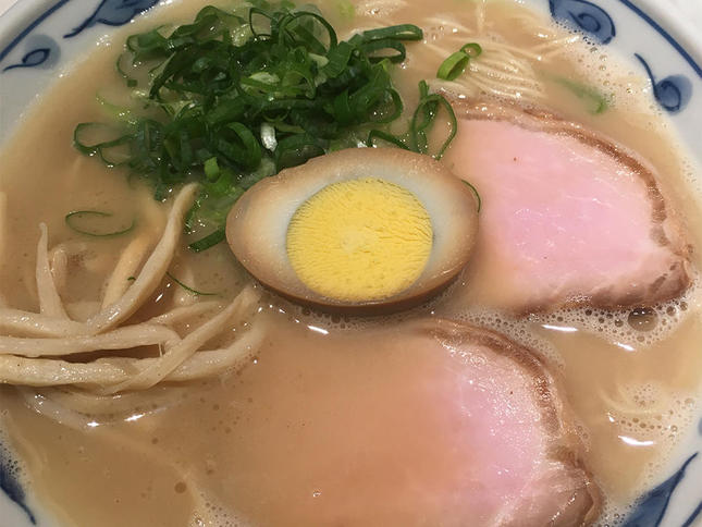 濁った茶色のスープの中に太麺と小ネギとチャーシューと煮卵がトッピングされたラーメン